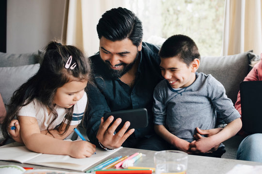Father showing mobile phone to children at home