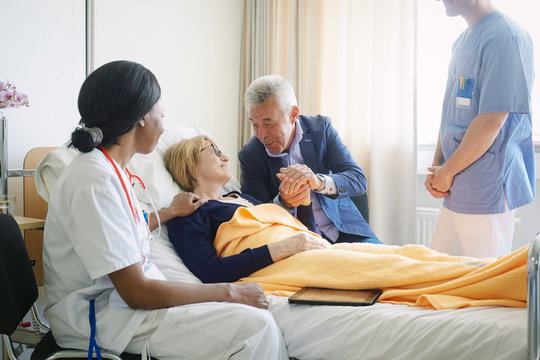 Healthcare workers looking at senior man consoling patient in hospital ward