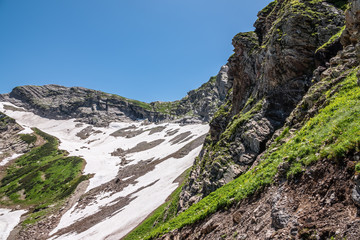 Mountain range with rocks and snow on slopes against a clear blue sky.