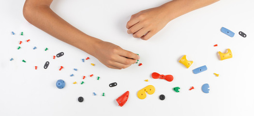 Kid hands playing with colorful plastic parts of constructor. Top view