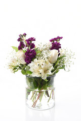 A beautiful floral arrangement in a clear glass vase on white with white roses and lilies.