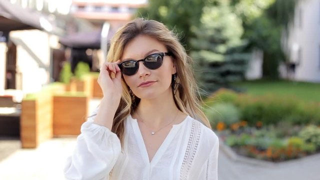 30s aged woman in white blouse taking off sunglasses. Slow motion