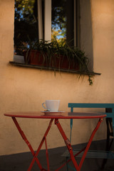 Street cafe - a round table with a cup of coffee on the background of a window with flowers on the windowsill