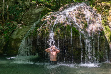 A man stands under the streams of water of a mountain waterfall
