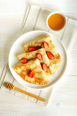 Crepes with strawberry and honey on white plate