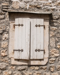 Old wooden window with white shatters on rough stone wall