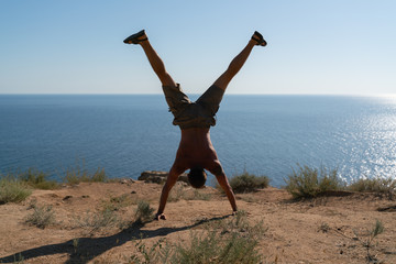 The guy stands on his hands, legs spread to the sides, against the background of the sea