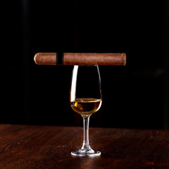 Smoking Cuban expensive cigar on the top of a tall glass with alcohol drink,single malt whiskey or cognac,luxury and classy lifestyle concept