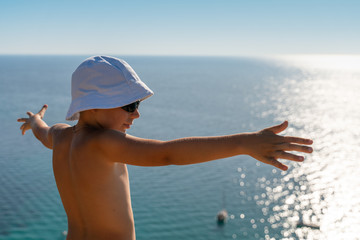 A child with outstretched arms, against the backdrop of the blue waters of the ocean