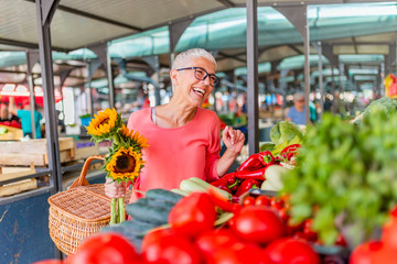  Senior woman shopping on the market healthy vegetables and fruits. Woman buying red peppers at the market. Woman buys fruits and vegetables at a market. Fresh and healthy food.