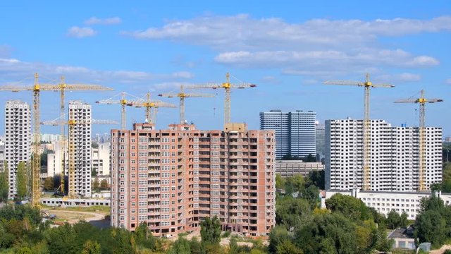 New housing estate in a big city. The construction of multi-storey buildings. Construction site with high cranes and building materials.