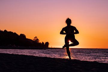 Fototapeta na wymiar Woman in yoga position in tree pose at sunset on the beach, zen, relax, calm and serene