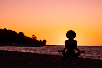 Fototapeta na wymiar Serene young woman meditating on the beach at sunset, facing the Pacific oceans with pink sky in the background, tranquil, zen, spiritual, wellbeing and healthy
