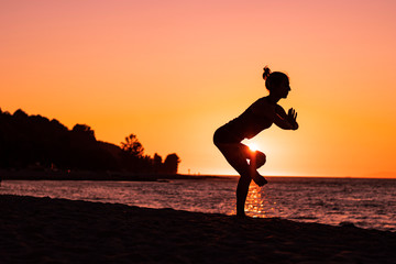 Woman doing yoga and exercises on the beach at the sunset, wellbeing, relaxation, serenity and health