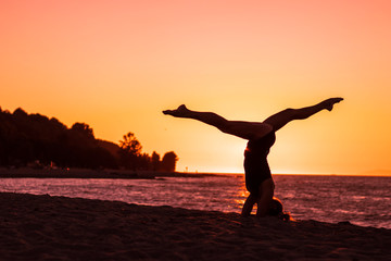 Fototapeta na wymiar Woman practicing ashtanga yoga on the beach at sunset with pink sky in background, zen attitude, serenity, healthy an wellbeing
