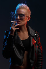 Portrait of a smoking blonde girl with stylish sunglasses on a dark background. Creative color. Studio photography.