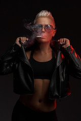 Portrait of a smoking blonde girl with stylish sunglasses on a dark background. Creative color. Studio photography.