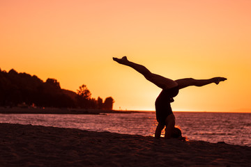 Fototapeta na wymiar Flexible woman practicing yoga and gymnastics on the beach at sunset, in utthita pose, wellbeing, good posture, zen attitude, healthy, ocean pacific view and tree shadow backgrounds