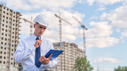 civil engineer in a white helmet makes pencil marks in the documentation.