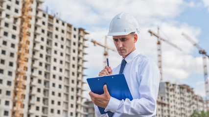 civil engineer in a white helmet makes pencil marks in the documentation.