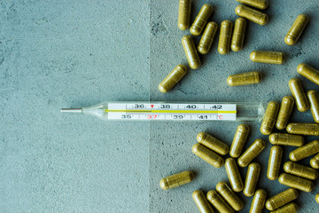 green biologically active food supplement scattered next to a transparent glass thermometer on a gray concrete background