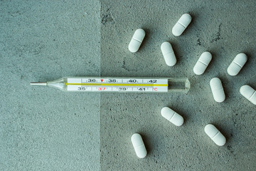  transparent glass thermometer with white yellow red pills vitamins capsules on gray concrete background