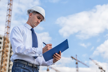 civil engineer in a white helmet on the background of construction, with a raised thumb.