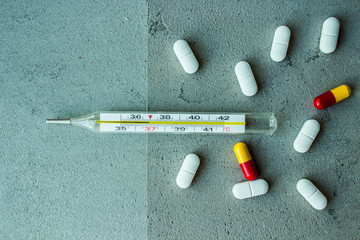  transparent glass thermometer with white yellow red pills vitamins capsules on gray concrete background