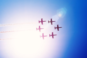 Aerobatic team group of fighters jet aircraft fly against the bright sun leaving a smoky trail in the air.