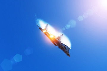Fototapeta na wymiar Combat fighter flies performing a maneuver in the air with clouds behind the wings, low pressure area. Sun glare from the bright sun and light from the nozzle of the afterburner.