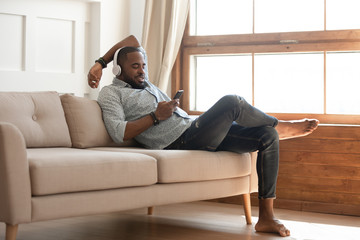 Black man relaxing on sofa at home, listen music.