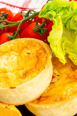 Two Small Fresh bakes Quiches on a Small Black Slate Tray  Fresh Vine Tomatoes  Cheddar Cheese and Lettuce on the side.