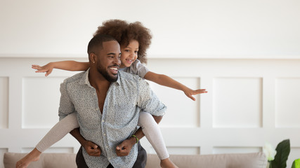 Excited black man giving piggyback ride to happy cute daughter.