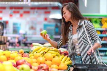 Woman chooses fresh green apple in fruit department of supermarket. Customer buying food at grocery...