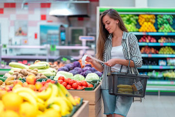 Young woman with shopping basket checks a sales receipt after purchasing food in a supermarket....