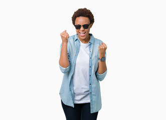 Beautiful young african american woman wearing sunglasses over isolated background very happy and excited doing winner gesture with arms raised, smiling and screaming for success. Celebration concept.