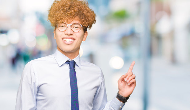 Young handsome business man with afro wearing glasses with a big smile on face, pointing with hand and finger to the side looking at the camera.