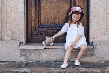 Cute little girl with her imaginary friend teddy bear, sitting alone.