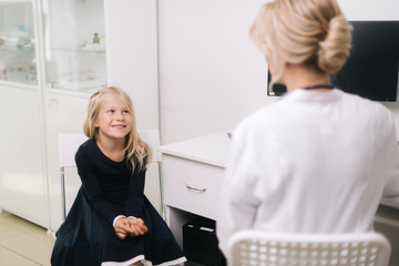 Cute smiling kid girl with blond hair at a pediatrician appointment. Little girl smiling at doctor appointment in bright office.