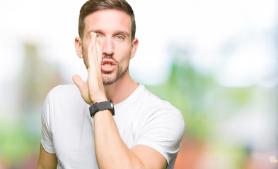 Handsome man wearing casual white t-shirt hand on mouth telling secret rumor, whispering malicious talk conversation