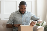 Happy young african american man unboxing delivery parcel.