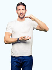 Handsome man wearing casual white t-shirt gesturing with hands showing big and large size sign, measure symbol. Smiling looking at the camera. Measuring concept.