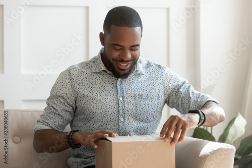 Happy young african american man unboxing delivery parcel.