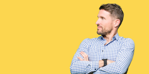 Handsome business man with blue eyes smiling looking to the side with arms crossed convinced and confident