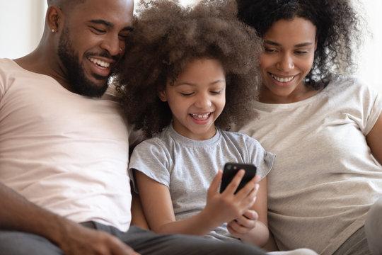 Happy african american parents watching little smiling kid playing game.