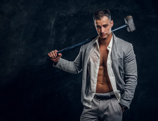 Young attractive hot man in suit and opened white shirt is holding long hammer in hand.