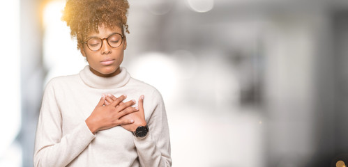 Beautiful young african american woman wearing glasses over isolated background smiling with hands on chest with closed eyes and grateful gesture on face. Health concept.