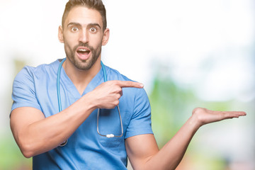 Handsome young doctor surgeon man over isolated background amazed and smiling to the camera while presenting with hand and pointing with finger.