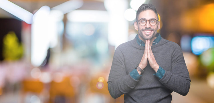 Young handsome man wearing glasses over isolated background praying with hands together asking for forgiveness smiling confident.
