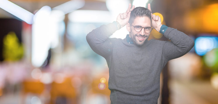 Young handsome man wearing glasses over isolated background Posing funny and crazy with fingers on head as bunny ears, smiling cheerful